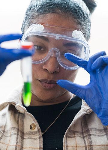 A chemistry student hold up a vial of green liquid